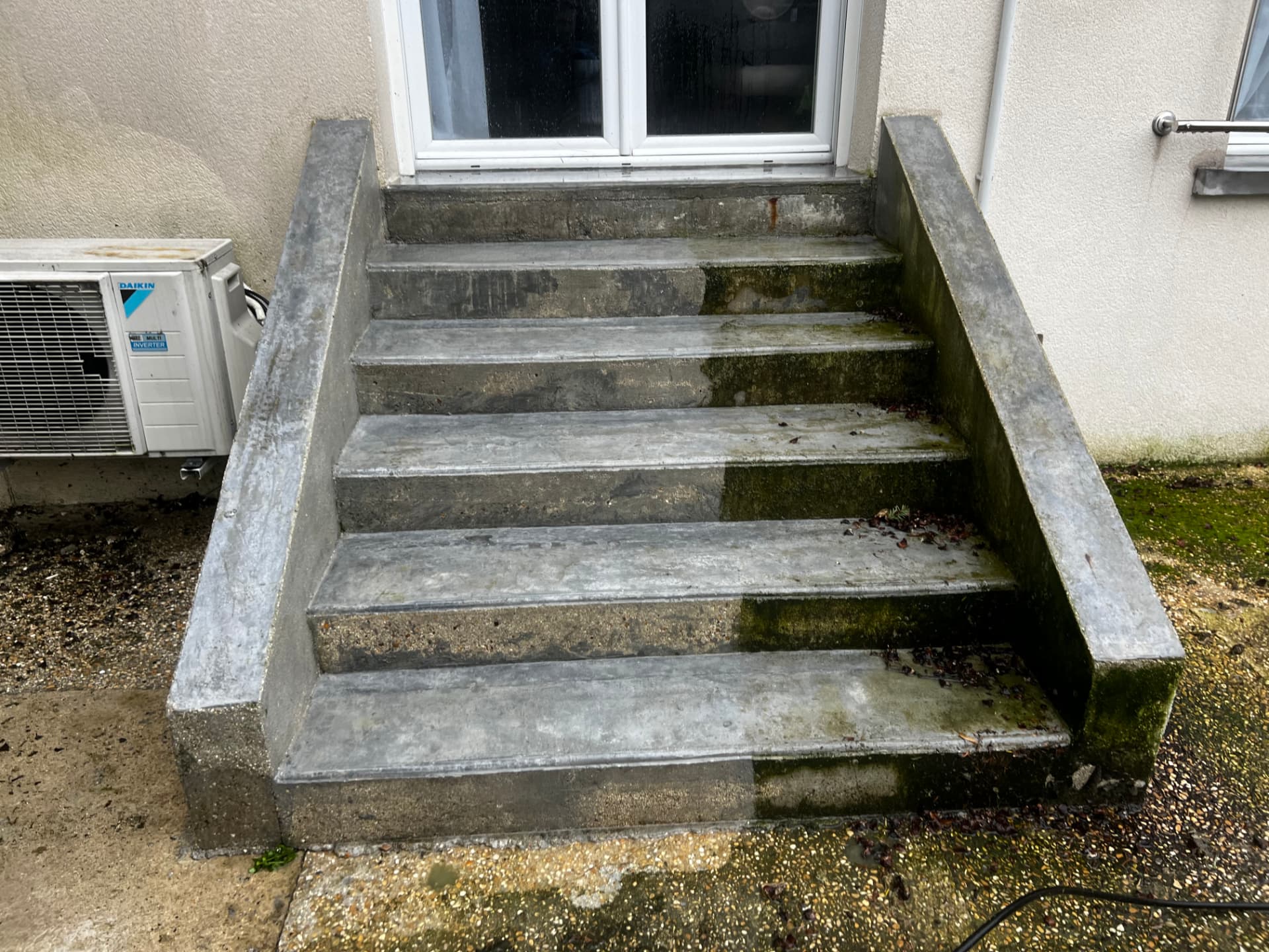 Escalier béton en cours de nettoyage haute pression, mousses et lichens éliminés à mi-parcours